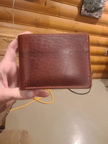 Customer holding the closed, brown Powell Bison Bifold wallet, showing the leather texture.