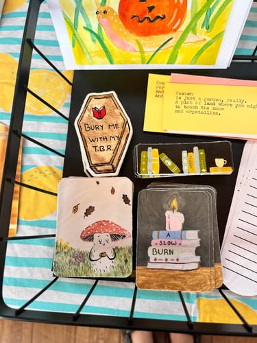 Reviewer's artistic custom vinyl stickers with book and mushroom themes displayed in a wire basket.