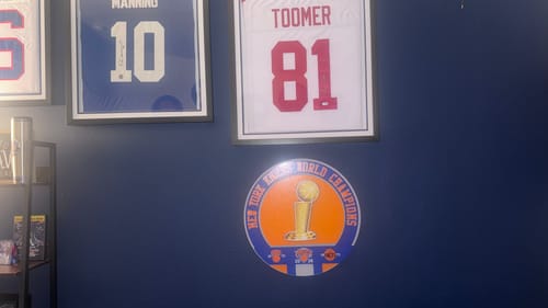 Customer's circular New York Knicks Champions artwork mounted on a dark blue wall below framed sports jerseys.