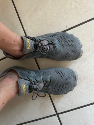 Rezensent trägt die grauen Smart Ⅰ Barfußschuhe auf einem Fliesenboden, von oben fotografiert.