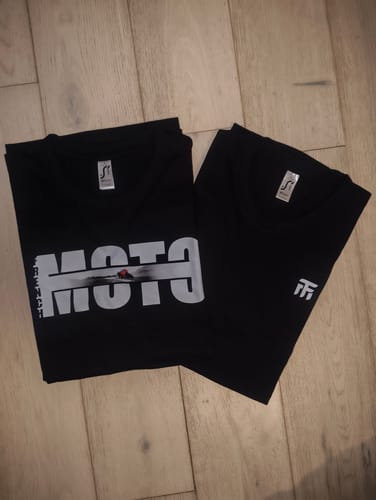 Client montrant ses deux modèles de t-shirts noirs COLLECTION PRISMA, pliés sur un sol en bois.