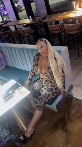 Customer sitting on a booth in a restaurant wearing the leopard print Naked Print Cutout Capri Jumpsuit.