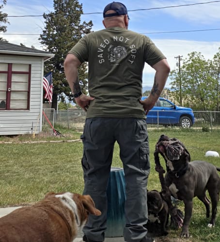 Customer seen from behind wearing the green Saved Not Soft T-Shirt, showing its athletic fit in a yard.