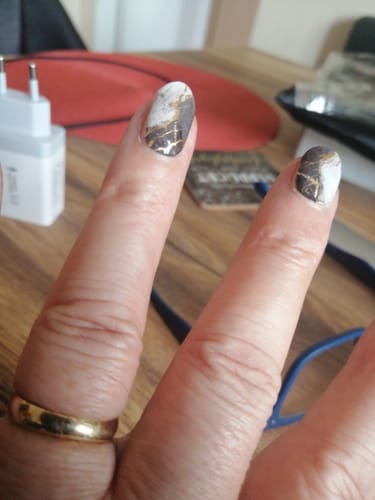 Hand einer Kundin, die ihre Nägel mit dem schwarz-weißen Refined Marble UV-Gel mit Goldakzenten zeigt.