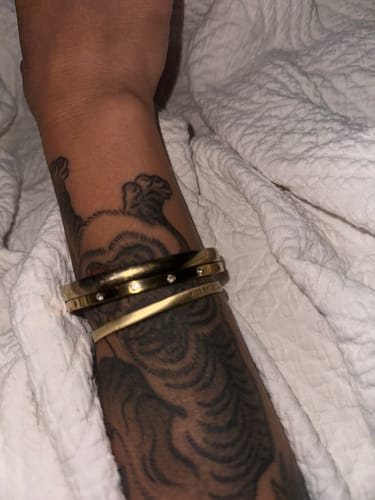 Reviewer's tattooed wrist wearing two stacked, gold-toned bracelets.