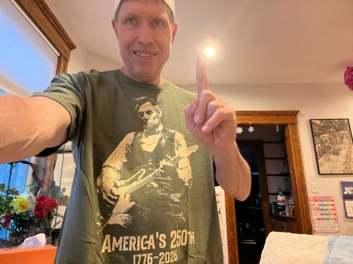 Reviewer smiling while wearing the green Lincoln 250 T-Shirt and holding up one finger.