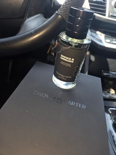 Customer's Smoke & Mirrors fragrance bottle resting on its premium black box inside a car.