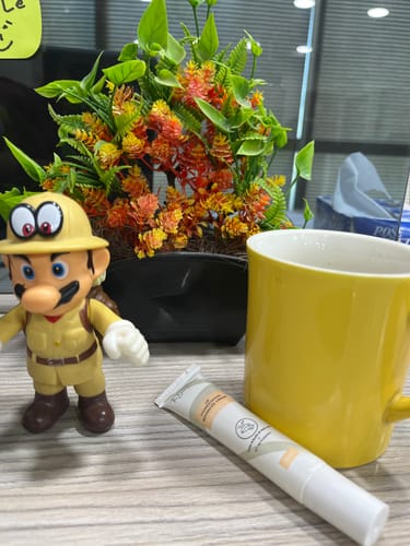 Customer's Advance Lip Pigmentation Cream on a desk next to a yellow mug, a plant, and a toy figurine.