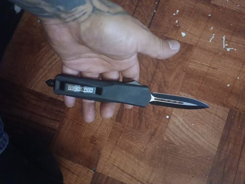 A customer's hand holding the black VIPER TEC GHOST OTF knife with its double-edged blade partially extended.