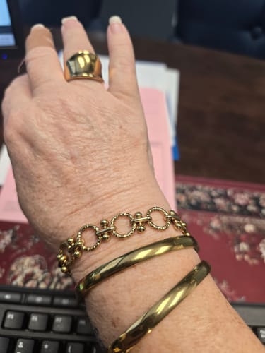 Customer shows their hand wearing four gold-colored pieces from the Waterproof Jewelry Bundle, including a ring and three bracelets.