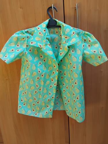 Customer's short-sleeved child's shirt made with the Avocado Hearts Polycotton Fabric, seen on a hanger.