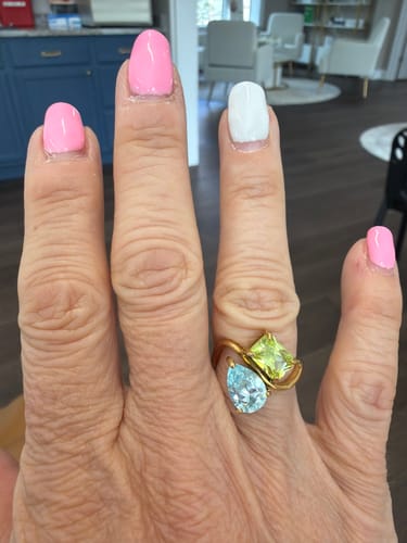 Reviewer's hand wearing the Navae Birthstone Ring with a light blue pear-shaped stone and a light green radiant-cut stone.