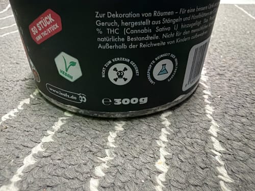 Kundenfoto einer Nahaufnahme des schwarzen Behälters, das Etiketten mit Warnhinweisen und dem Vegan-Symbol zeigt.