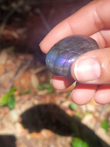 Close-up of a customer's hand holding a dark, polished crystal with a purple sheen, used with the Crystal Comfort Card Deck.