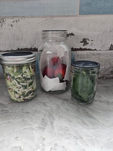 Customer's three mason jars of fresh produce like strawberries and salad, sealed using the Mason Genie Vacuum Sealer.