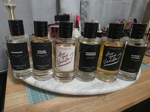 Customer's Suede & Stone Eau de Parfum bottle, part of a large collection displayed on a white marble tray.