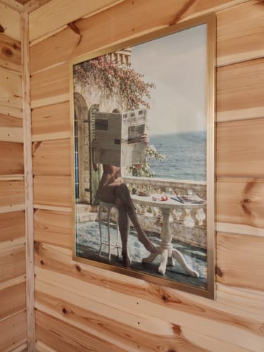 Customer's La Dolce Niente N02 art print in a gold frame hung on a light wood-paneled wall.