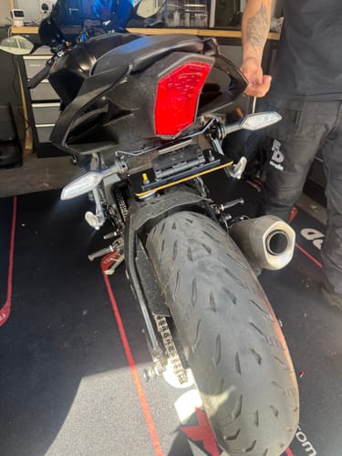 Customer's black motorcycle in a workshop, with a technician performing the Bracket Fitment Service on the rear indicators and plate.