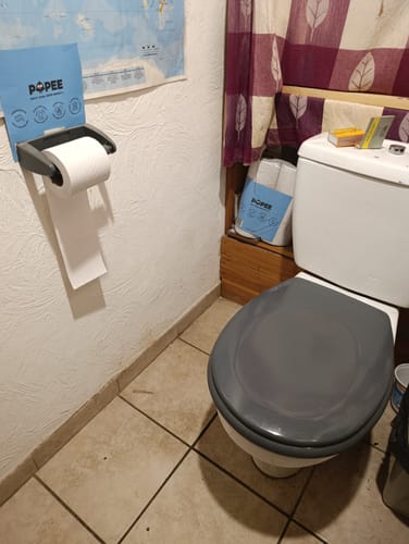 Client montrant le papier toilette compact en position sur le support mural dans une salle de bain.