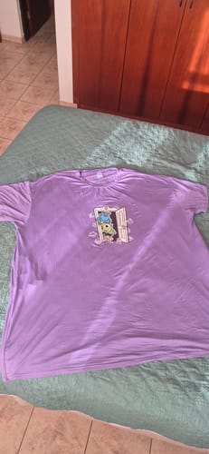 Cliente mostrando a camisola roxa com estampa de Monstros S.A. aberta sobre uma cama.