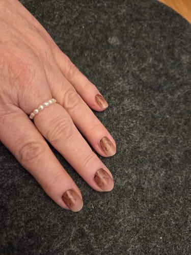 Hand einer Kundin, die ihre Nägel mit den 'Neutral Love' UV-Gel-Nagelfolien in einem braunen Design auf einer dunklen Oberfläche zeigt.