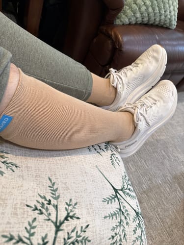 Reviewer relaxing with feet up, wearing the tan Eucalyptus Lyocell Compression Socks with white sneakers.
