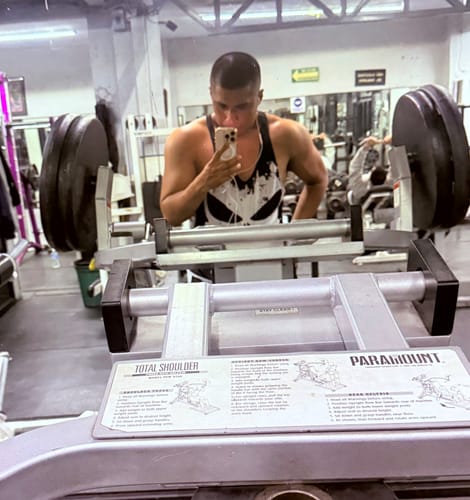Cliente en el gimnasio mostrando su físico musculoso en un espejo.