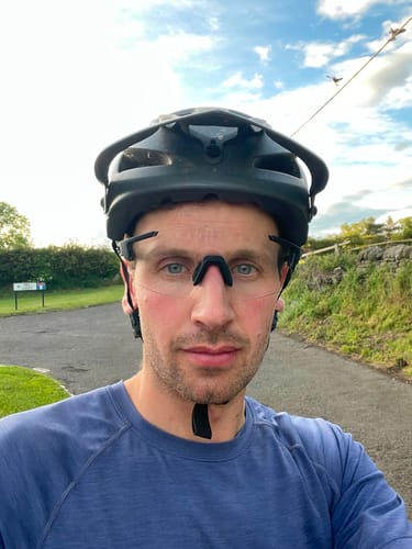 Reviewer wearing frameless Deathray™ Riding Glasses with a clear lens and a helmet outdoors.