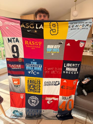 Customer holding a large, colorful Project Repat T-Shirt Quilt made from various sports and school t-shirts.