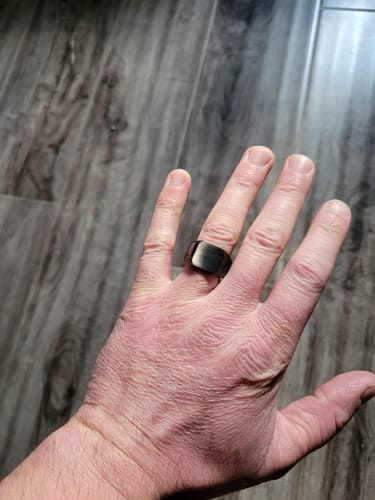 A reviewer wearing the matte black Signet Ring on their hand against a wood-grain floor.