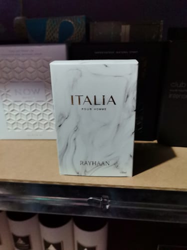 Un cliente muestra la caja blanca y marmolada del perfume Rayhaan Italia sobre un estante.