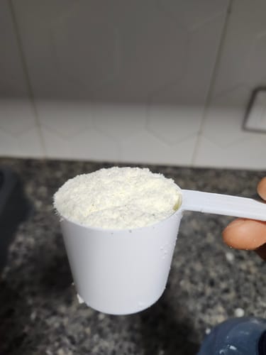 Cliente sostiene una cuchara medidora llena de polvo fino de Proteína Aislada (ISO).