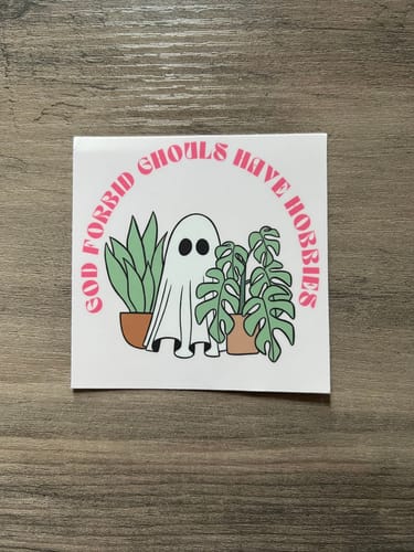 Customer's square custom sticker with a cartoon ghost and plants, reading 'God Forbid Ghouls Have Hobbies' in pink text.