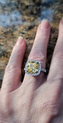 Customer wearing the canary yellow cushion cut halo ring on their finger against a granite background.