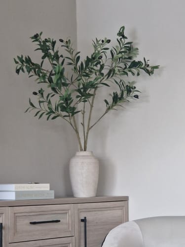 Customer's two Faux Olive Oversized Branches arranged in a light-colored vase on a wooden cabinet.