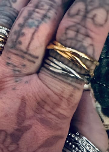 Close-up of a reviewer's tattooed finger wearing the gold Spins Tidal Roller Ring stacked with a silver one.