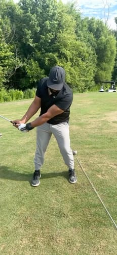 A reviewer mid-swing at a driving range, wearing the black FlexClick training aid on their lead wrist to improve their form.