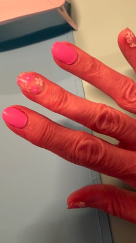 Close-up of a customer's hand with bright pink nails and floral accent nails using the Holy Gels kit.
