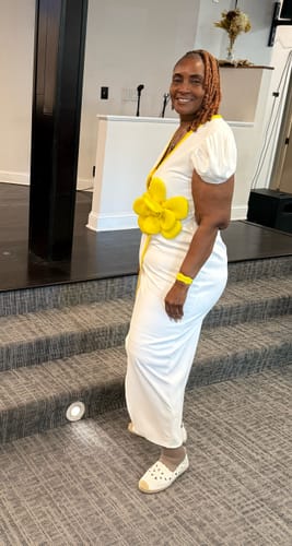 Reviewer standing sideways in a white maxi dress with puffy sleeves and a large yellow flower.