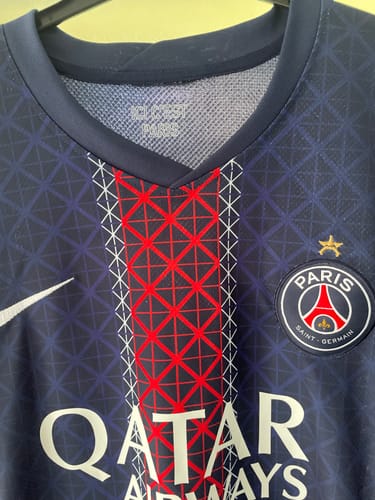 Gros plan sur le col et l'écusson du Maillot 25/26 PSG Domicile.