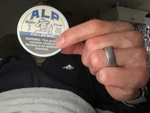 A reviewer's hand holding a round can of Chilled Mint Nicotine Pouches, showing the label.