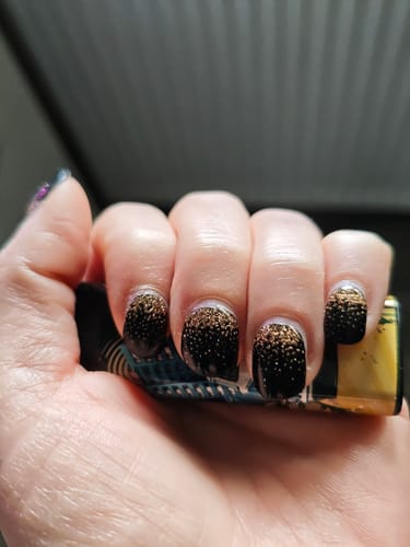Nahaufnahme der Hand einer Kundin, die die leicht herausgewachsenen 'Midnight Gold Ombré' UV-Gel-Nägel zeigt.