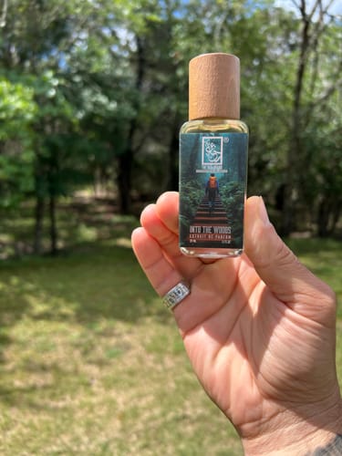 Customer holding a Dua Into The Woods extrait bottle with a wooden cap outdoors