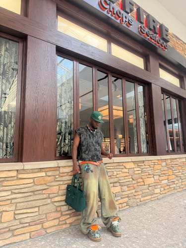Customer wearing the baggy Gradient Sandwash Jeans outdoors with a sleeveless shirt and green bag.