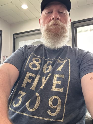 Reviewer wearing the dark grey 8675309 T-Shirt with gold distressed print.