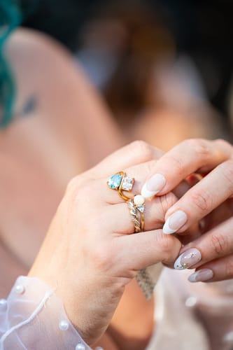 A reviewer's hand wearing the gold Navae Birthstone Ring, showing its pear-cut blue and radiant-cut clear stones.