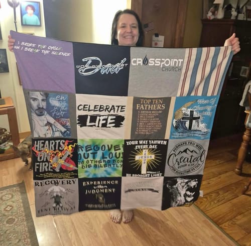 Customer proudly holding up her large Project Repat T-Shirt Quilt, showing the collection of memorial shirts.
