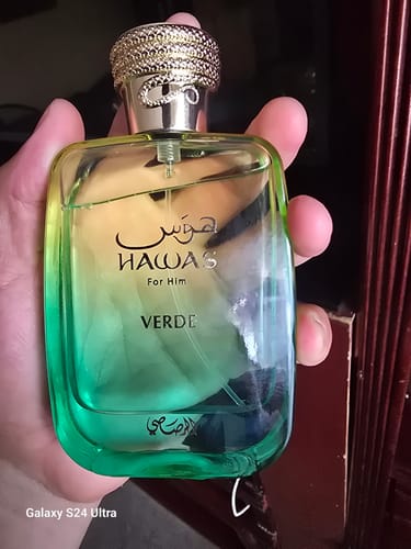 Un cliente sostiene en su mano el perfume Rasasi Hawas Verde, mostrando el frasco de cristal degradado y la tapa dorada.