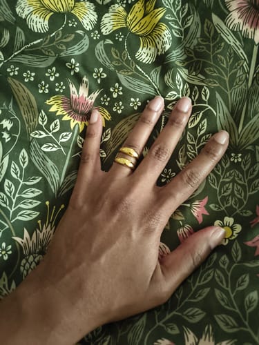 Customer's hand wearing the bold, gold Sunstone Ring on their finger against a floral background.