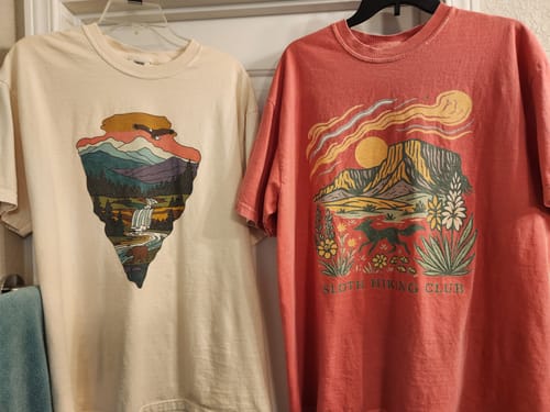 Customer's off-white Arrowhead T-Shirt with a nature graphic shown hanging next to another tee.